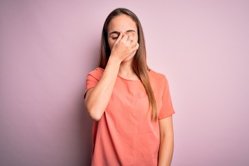 Young beautiful woman wearing casual t-shirt standing over isolated pink background tired rubbing nose and eyes feeling fatigue and headache. Stress and frustration concept.