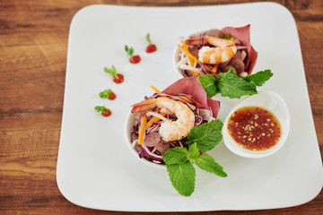 Two small bowls of vegetable salad decorated with shrimps and small dish with tasty dressing