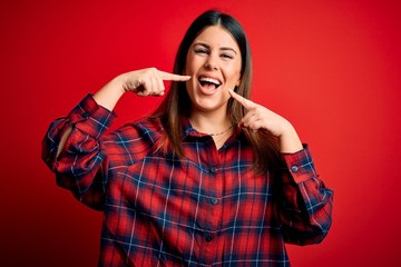 Young beautiful woman wearing casual shirt over red background smiling cheerful showing and pointing with fingers teeth and mouth. Dental health concept.