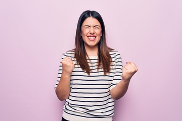 Young beautiful brunette woman wearing casual striped t-shirt over isolated pink background celebrating surprised and amazed for success with arms raised and eyes closed