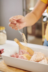 Woman adding tea spoon of species in cooking tray with ground pork and chicken