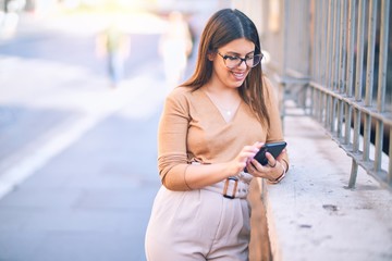 Fototapeta premium Young beautiful woman smiling happy and confident. Standing with smile on face using smartphone at the city