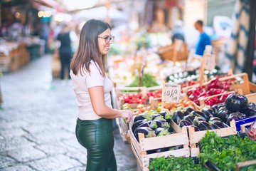 Young beautiful woman smiling happy and confident. Standing with smile on face looking at greengrocery at the town street