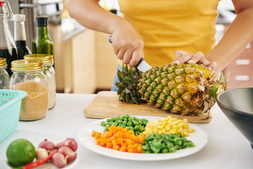 Cropped image of woman cutting fresh ripe pineapple and making tasty dish for dinner when cooking during lockdown