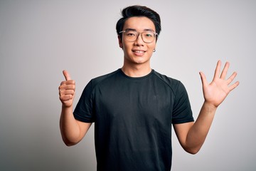 Young handsome chinese man wearing black t-shirt and glasses over white background showing and pointing up with fingers number six while smiling confident and happy.