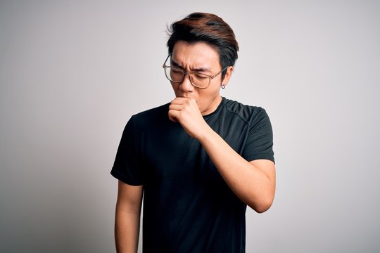 Young Handsome Chinese Man Wearing Black T-shirt And Glasses Over White Background Feeling Unwell And Coughing As Symptom For Cold Or Bronchitis. Health Care Concept.