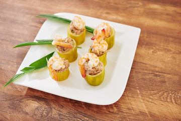 Square plate with stuffed zuccini rings decorated with shrimps on wooden table