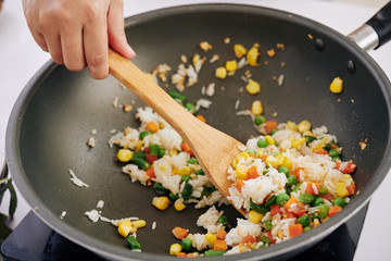 Close-up image of woman frying rice with vegetables in wok frying pan