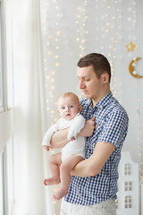 Little Boy with his fother weared in pajamas near window. Happy family in light scandinavian children's room. Good morning of Dad & infant son in sleepwear. Stay home concept. Relationship with love