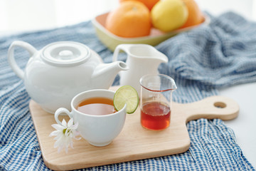 Cup of tasty herbal tea with slice of lime and teapot on wooden cupboard