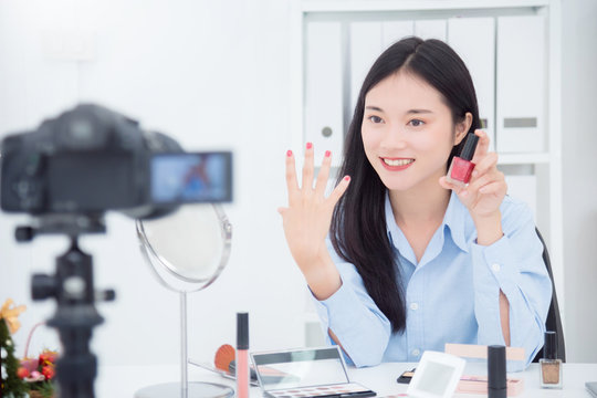 Beautiful asian girl holding nail polish bottle and showing her nail color in front of camera to recording vlog video live streaming at her shop.