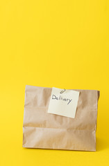 Craft paper bag for takeaway on yellow background. Delivery service concept.
