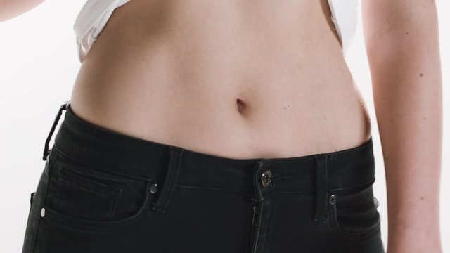 Close-up of a woman's stomach as she holds up her shirt to show off her slim waist.
