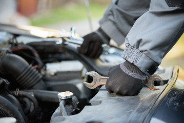 Auto mechanic with wrenches is standing near car open hood close up.