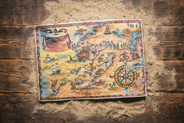 Pirate treasure map on sand on brown wooden table flat lay background.