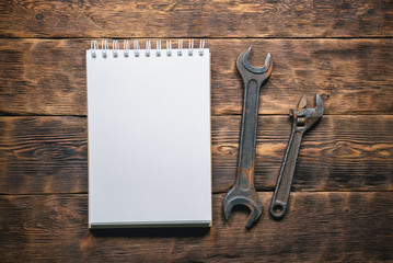 Old wrenches and blank page notepad on brown wooden workbench background. Fix list.
