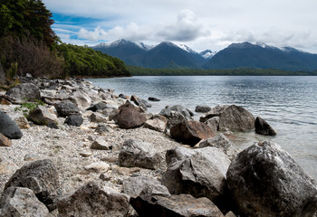 Rocky shore of the lake with mountains in backdrop, shot at lake Manapouri, Fiordland National Park, New Zealand