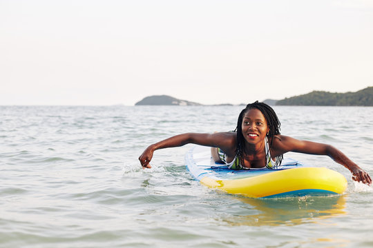 Pretty young Black woman enjoying swimming on surfboard in sea