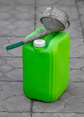 Green plastic canister with gasoline and a funnel for filling.