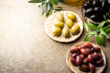 Black and green olives and olive oil in bowls on stone background. Top view with copy space for text.
