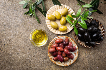 Black and green olives and olive oil in bowls on stone background. Top view with copy space for...