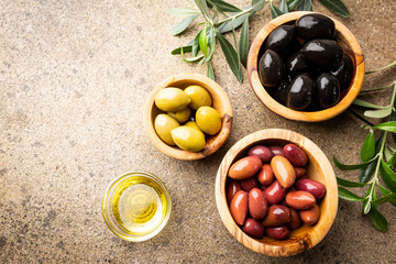 Black and green olives and olive oil in wooden bowls on stone background. Top view with copy space...