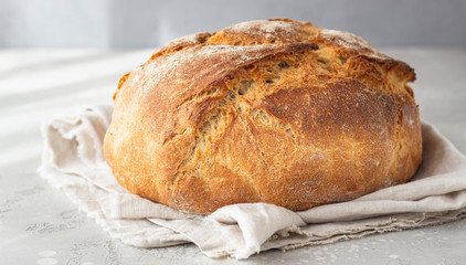 Whole artisan rustic bread from wheat and rye flour on a linen napkin, light grey stone background. Selective focus. 