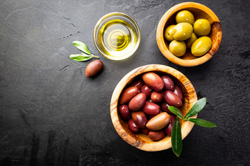 Black and green olives and olive oil in wooden bowls on black background. Top view with copy space...