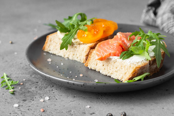 Open sandwiches with wheat and rye bread, tomatoes, smoked salmon and arugula, grey concrete background. Selective focus. 