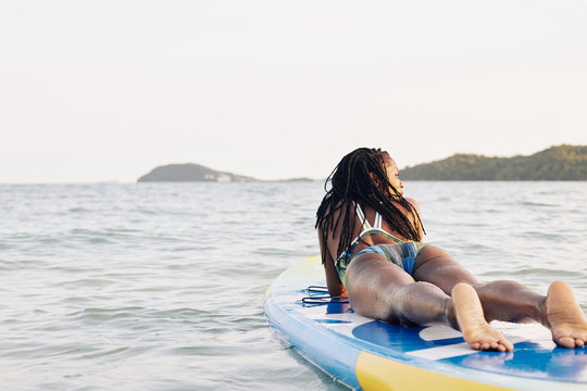 Happy young Blask woman relaxing on sup surfing board after swimming in ocean