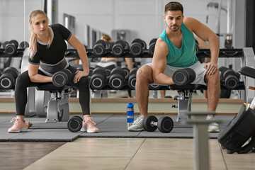 Fototapeta na wymiar Sporty young couple training with dumbbells in gym