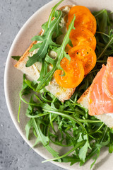 Healthy open sandwiches with artisan bread with cream cheese, salmon, tomatoes and arugula on ceramic plate. Balanced diet concept. Top view.