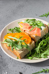 Healthy open sandwiches with artisan bread with cream cheese, salmon, tomatoes and arugula on ceramic plate. Balanced diet concept. 