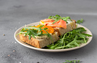 Healthy open sandwiches with artisan bread with cream cheese, salmon, tomatoes and arugula on ceramic plate. Balanced diet concept. 