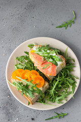 Healthy open sandwiches with artisan bread with cream cheese, salmon, tomatoes and arugula on ceramic plate. Balanced diet concept. Top view.