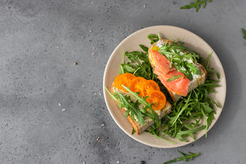 Healthy open sandwiches with artisan bread with cream cheese, salmon, tomatoes and arugula on ceramic plate. Balanced diet concept. Top view.