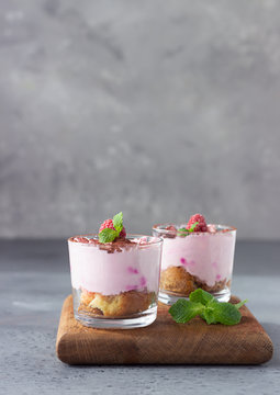 Pink layered dessert trifle, tiramisu or parfait with raspberries and mint decorated with cocoa powder in glasses. No bake summer dessert. Grey concrete background.