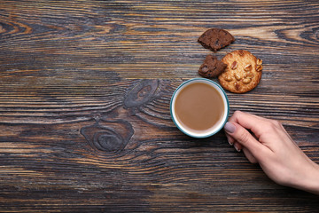 Female hand with cup of coffee and cookies on wooden background