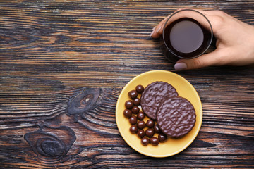 Female hand with glass of coffee and sweets on wooden background