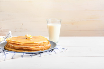 Tasty blini with butter and milk on table