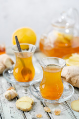 Ginger tea in a glass cup with lemon and mint on light background