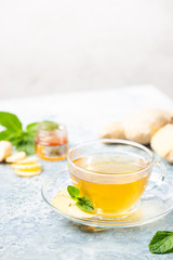 Ginger tea in a glass cup with lemon and mint on light background