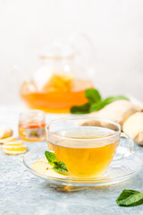 Ginger tea in a glass cup with lemon and mint on light background