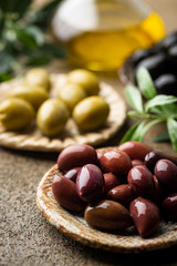 Variety of black and green olives and olive oil in bowls on stone background close up