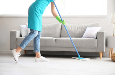 Young woman mopping floor in room