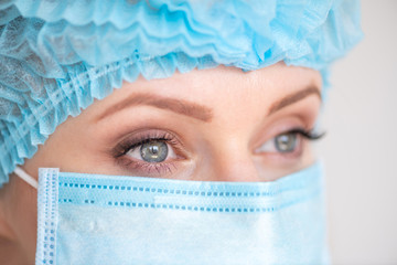 Nurse or doctor with face mask and cap. Close up portrait of young caucasian woman model on white background