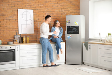 Happy couple near chalkboard with written menu on refrigerator in kitchen