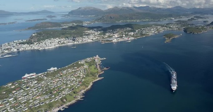 Extremely cinematic, high altitude aerial footage of a luxurious cruise ship sailing in a fjord next to Alesund, the most beautiful Art Nouveau town in Norway.
