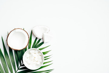 Coconut fruit with half and grated coconut in bowl, tropical palm leaf on white background. Flat lay, top view. Summer background.