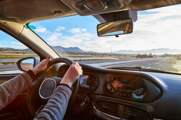 Windscreen view of nature, road, sun and hand of woman on the steering wheel in a spring, summer or...
